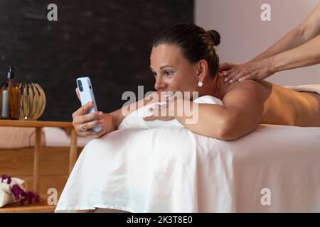 Mature woman using the mobile phone while getting a massage in a spa Stock Photo