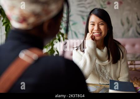 Two multicultural female students sitting in cafeteria and study for exam. Stock Photo