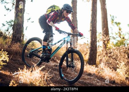 Side view of woman with backpack riding on bicycle on path between trees on hill in forest Stock Photo