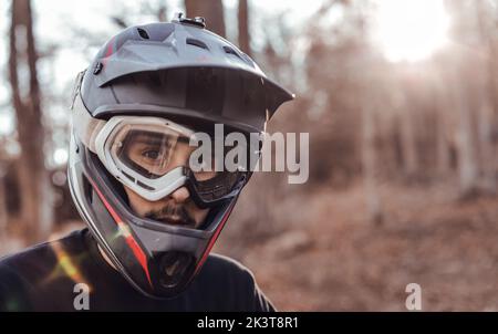 Young guy in safety helmet and sport glasses looking at camera in forest on blurred background Stock Photo
