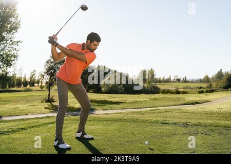 Professional male golf player preparing to hit ball with putter in green field while looking down on summer day Stock Photo