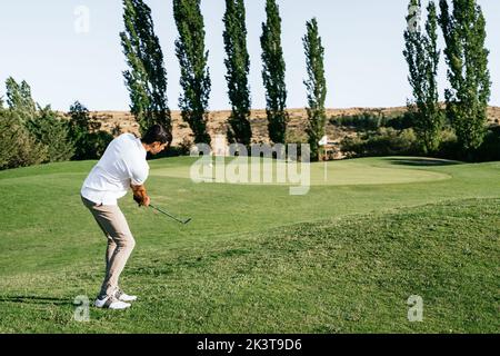 Professional male golf player preparing to hit ball with putter in green field while looking down on summer day Stock Photo