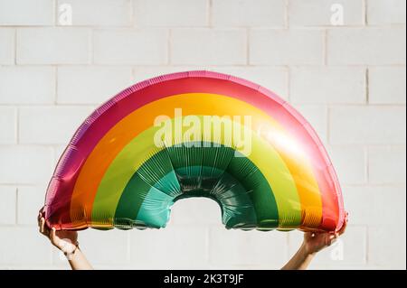 Crop anonymous person holding bright multicolored inflatable rainbow mattress for swimming in pool against white wall Stock Photo