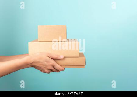 Stack of cardboard boxes in female hands. Blank brown parcel boxes on light blue background. Mock up. Packaging, shopping, free shipping, delivery Stock Photo