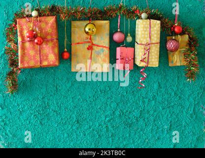 Christmas gifts, presents hanging on teal background with decoration, christmas balls wrapped gift boxes.Template, negative space technique,large copy Stock Photo
