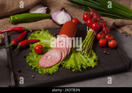 tasty smoked servelat on a wooden board decorated with fresh vegetables Stock Photo