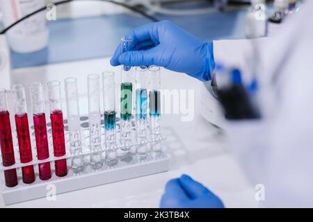 Crop close up view of hand of anonymous researcher taking tube from a set of test flasks with color liquids at laboratory Stock Photo