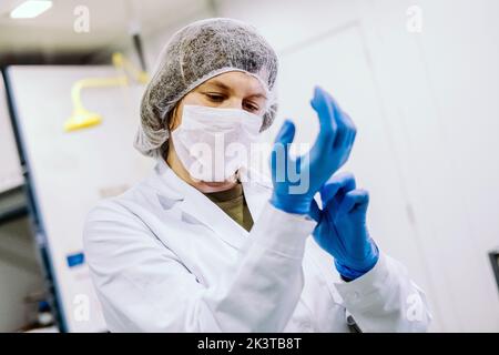 Young woman in glasses standing in modern laboratory and putting on gloves. Stock Photo