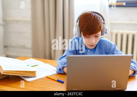 Photo of a pupil boy during an online lesson in front of a laptop monitor. He writes an online message to the teacher. Online learning concept. Stock Photo