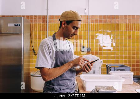Young male business owner using mobile phone and making order to supplier while working in bakery Stock Photo