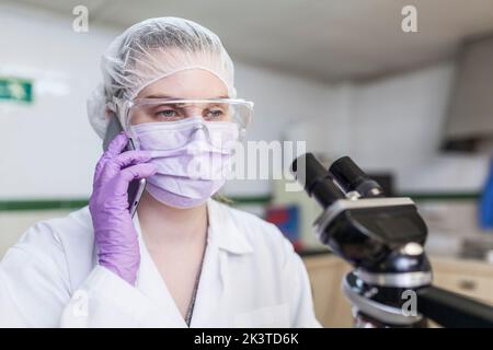 woman working at a lab using a smartphone next to a microscope at a laboratory Stock Photo