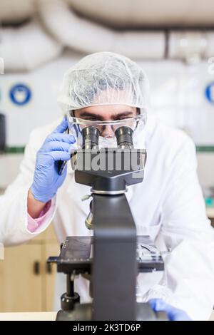 Man working at a lab using a smartphone while using a microscope at a laboratory Stock Photo