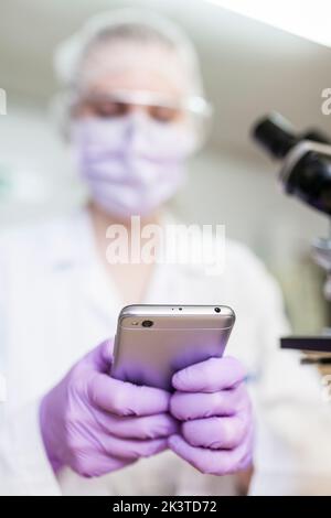 woman working at a lab using a smartphone next to a microscope at a laboratory Stock Photo
