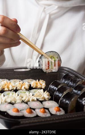a girl in light clothes eats tasty rolls from a container Stock Photo