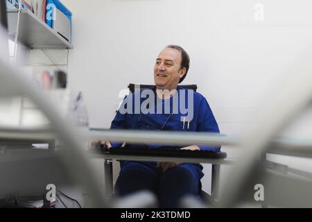 Adult cheerful male doctor in uniform working at computer in veterinary clinic Stock Photo