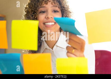 Through glass view of crop content ethnic female worker catching colorful sticky notes on wall in office Stock Photo