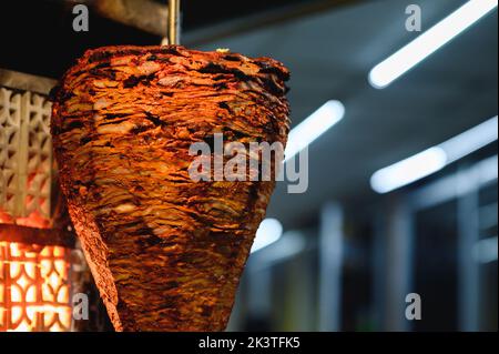 Vertical broiler with tasty meat against shiny lights in restaurant kitchen on blurred background Stock Photo
