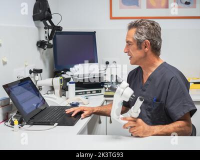 Side view of mature man with microscope browsing laptop while working in modern medical laboratory in hospital Stock Photo