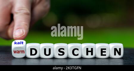 Hand turns dice and changes the German expression 'warm duschen' (warm shower) to 'kalt duschen' (cold shower). Stock Photo
