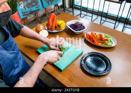 Crop anonymous chef chopping fresh green parsley on cutting board while cooking in kitchen Stock Photo