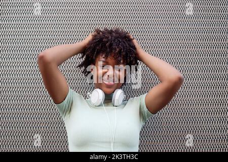 Young mixed race woman with afro hairstyle smiling in urban background. Black girl in casual clothes. Stock Photo