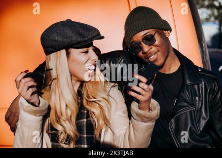 Handsome African American guy smiling and hugging beautiful laughing female with mascara while standing on street together Stock Photo
