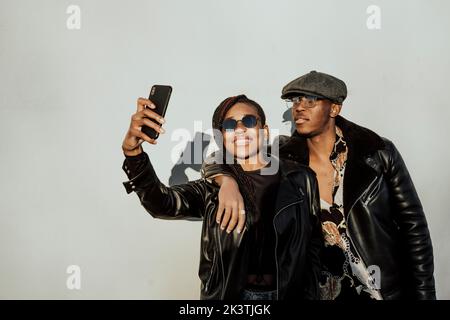 Afro couple making a self portrait in the street next to a white wall on a sunny day Stock Photo