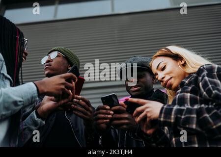 From below young African American people browsing modern smartphones while standing on city street together Stock Photo