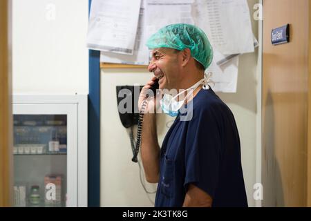 Side view of adult man in surgeon uniform laughing while talking on phone in hospital Stock Photo