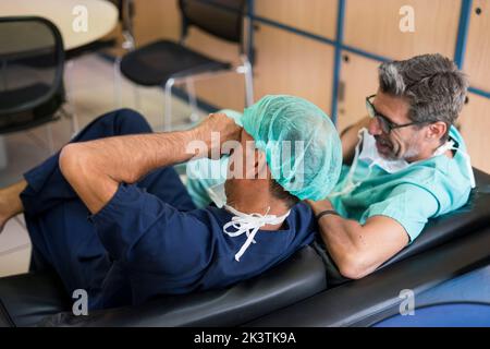 From above shot of two men in surgeon uniform laughing while sitting on comfortable sofa in office Stock Photo