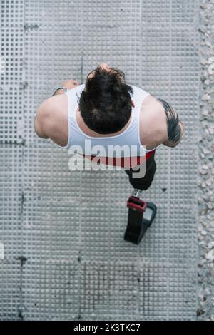 from above young guy with leg prosthesis running up paved slope against shabby building during workout on city street Stock Photo
