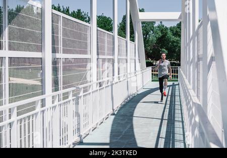 young guy with leg prosthesis running on bridge during workout on city street Stock Photo