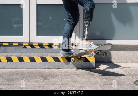 From below young guy with leg prosthesis jumping on skateboard above ground against modern building on sunny day Stock Photo