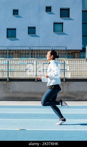 Side view of strong sportswoman running on blue racetrack fast during track and field training on stadium Stock Photo
