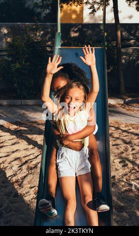 friendly active diverse girls having fun at slide in bright day Stock Photo