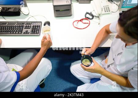 From above doctors in white uniform sitting near table in office and drinking coffee while working in hospital together Stock Photo