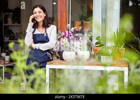 Cheerful young adult female entrepreneur talking on smartphone Stock Photo