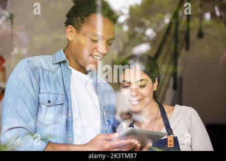 Small business owners standing behind window while using digital tablet Stock Photo