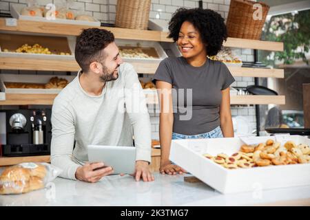 Bakery coworkers smiling at each other while standing behind counter Stock Photo