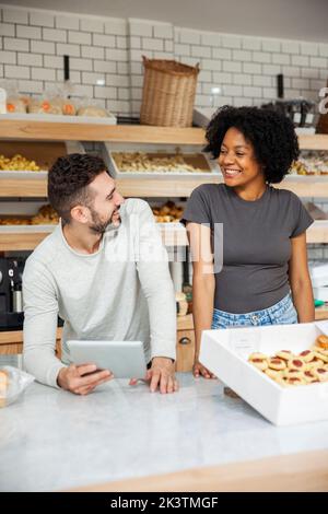 Bakery owners looking at each other while standing behind counter Stock Photo