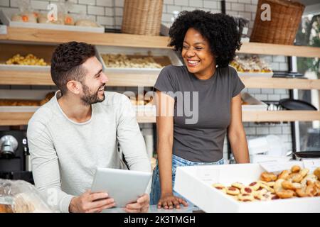 Bakery coworkers looking at each other while standing behind counter Stock Photo