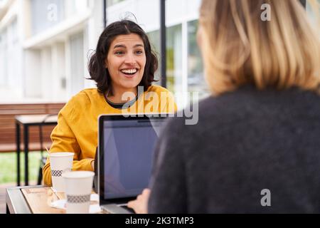 Mid-shot of two smiling female co-workers discussing business matters outdoors Stock Photo
