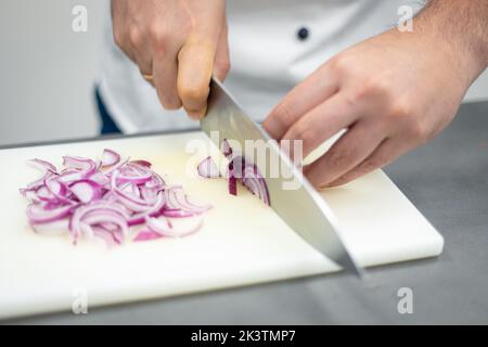 Crop man in white chef jacket cutting onion with knife on white cutting board Stock Photo
