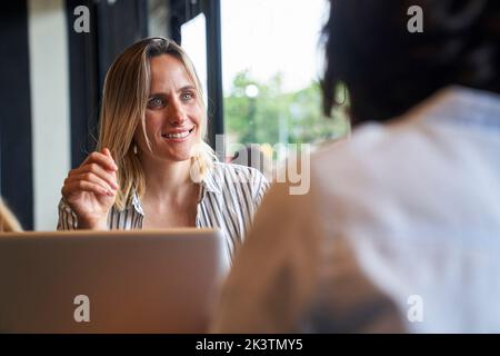 Mid-shot of two female co-workers discussing work matters at company's cafeteria Stock Photo