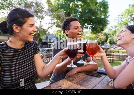Mid-shot of ethnically diverse group of friends celebrating and making a toast while drinking homebrewed beer Stock Photo