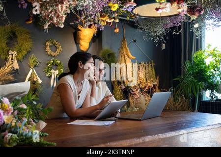 Wide view of two diverse female home decoration shop owners working with laptop computer and digital tablet Stock Photo