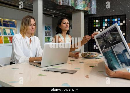 Two young female home decor entrepreneurs sitting at their desk with a client Stock Photo