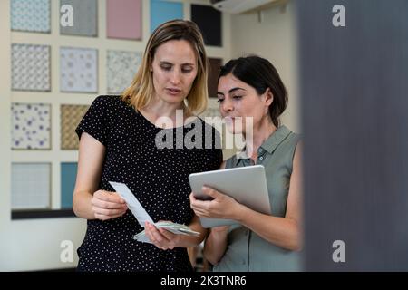 Medium shot of two female home decoration business owners choosing colors from color swatches Stock Photo