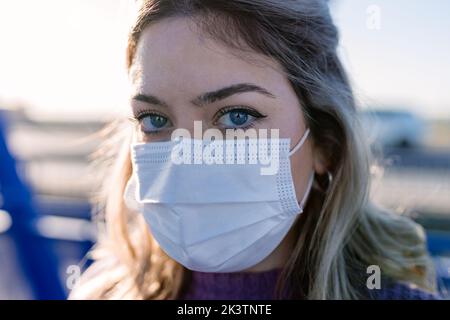 Serious female wearing protective mask standing on metal footbridge in city and looking at camera Stock Photo