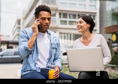 Mid-shot of diverse couple of co-workers discussing business matters while working outdoors Stock Photo